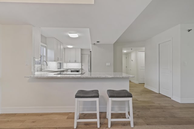 kitchen with tasteful backsplash, light stone counters, a peninsula, light wood-type flooring, and white cabinetry