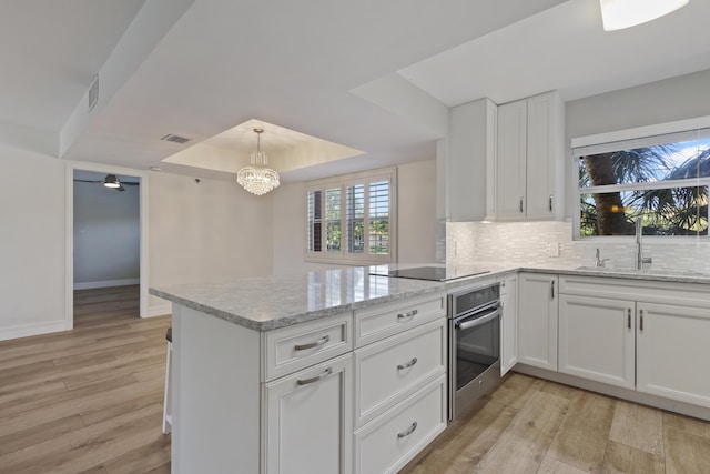 kitchen with black electric stovetop, a raised ceiling, a sink, oven, and a peninsula