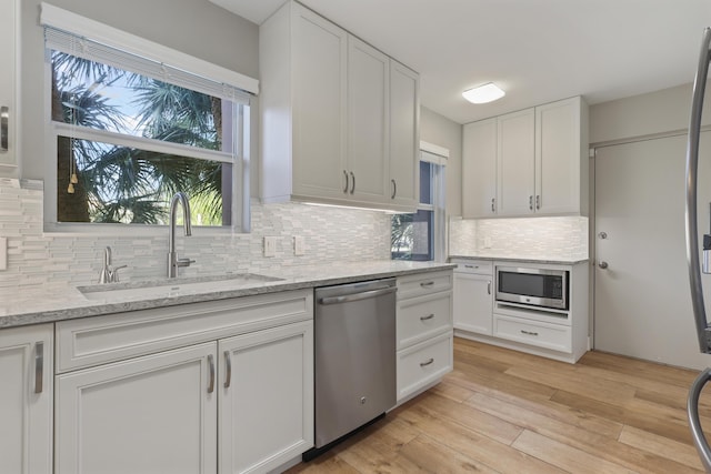 kitchen with light stone countertops, appliances with stainless steel finishes, tasteful backsplash, sink, and white cabinets