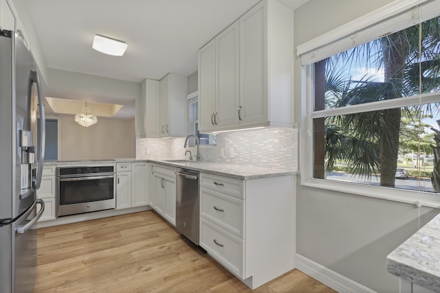 kitchen featuring appliances with stainless steel finishes, light wood-type flooring, a sink, and decorative backsplash