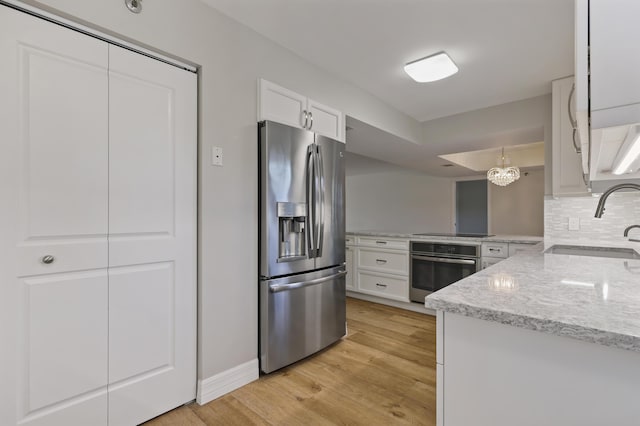 kitchen featuring light wood finished floors, appliances with stainless steel finishes, a sink, white cabinetry, and backsplash