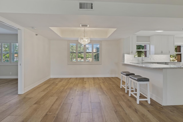 unfurnished dining area with light wood-style flooring, a notable chandelier, visible vents, baseboards, and a raised ceiling