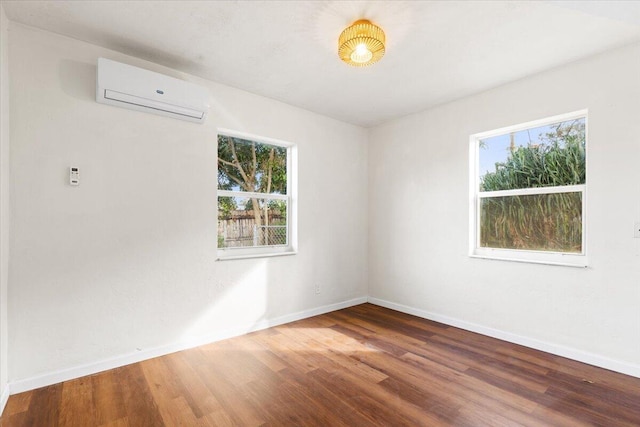 empty room featuring a wall mounted air conditioner, a healthy amount of sunlight, and hardwood / wood-style flooring