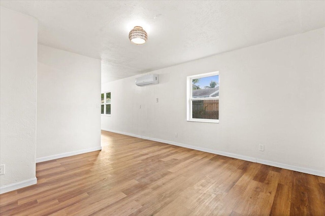 spare room featuring a wall mounted air conditioner, a textured ceiling, and light hardwood / wood-style floors