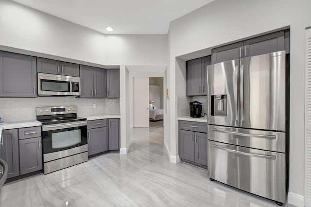 kitchen featuring gray cabinetry, decorative backsplash, stainless steel appliances, and a high ceiling