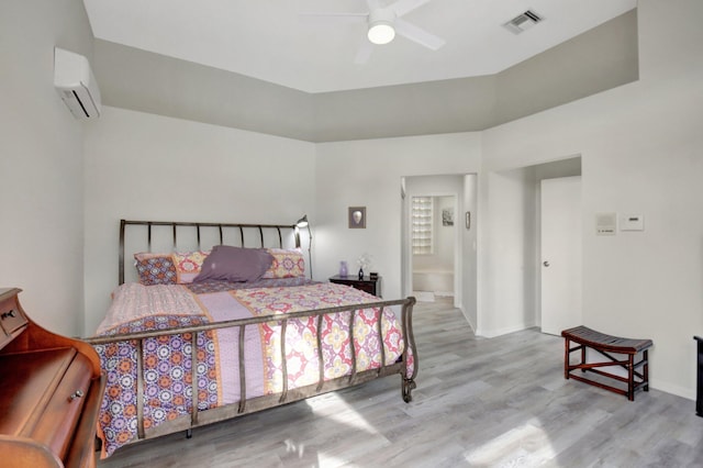 bedroom with ceiling fan, light wood-type flooring, a wall unit AC, and connected bathroom