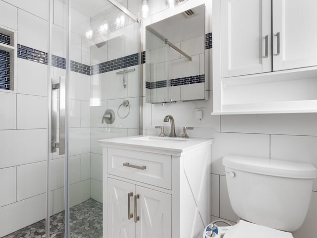 bathroom with vanity, toilet, tile walls, and a shower with shower door