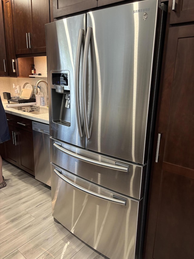 kitchen with dark brown cabinetry, sink, stainless steel appliances, light hardwood / wood-style floors, and backsplash