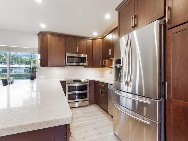 kitchen with appliances with stainless steel finishes, light stone countertops, light hardwood / wood-style floors, and decorative backsplash