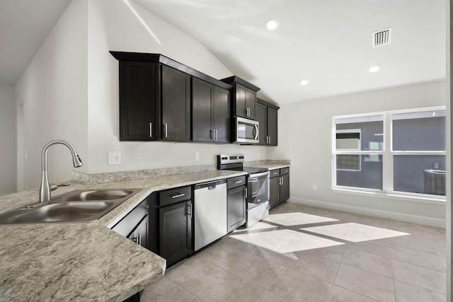 kitchen with lofted ceiling, sink, light stone countertops, light tile patterned floors, and stainless steel appliances