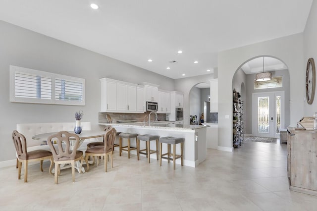 kitchen with kitchen peninsula, appliances with stainless steel finishes, decorative backsplash, light stone countertops, and white cabinetry