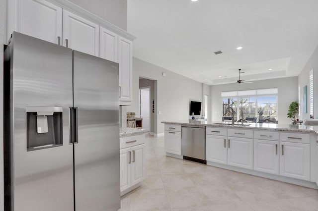 kitchen with white cabinets, stainless steel appliances, light stone counters, and a tray ceiling