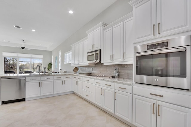 kitchen with backsplash, white cabinets, ceiling fan, light stone countertops, and stainless steel appliances