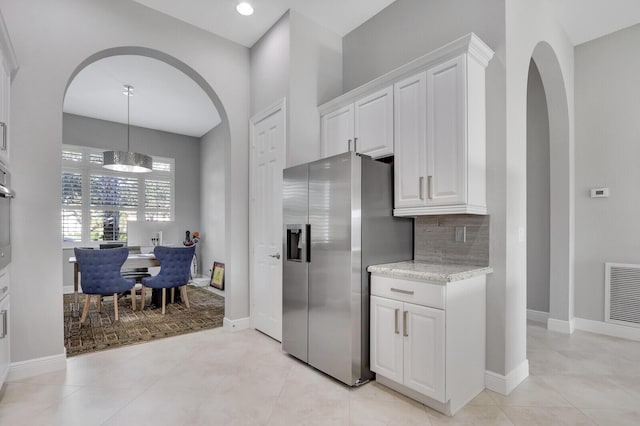 kitchen featuring decorative backsplash, stainless steel refrigerator with ice dispenser, light stone countertops, a chandelier, and white cabinetry