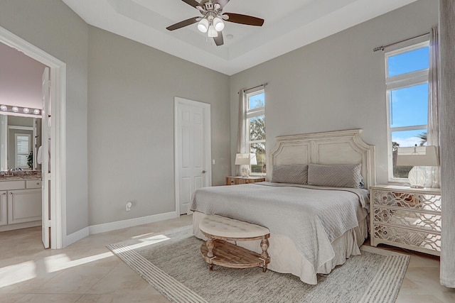 bedroom with a tray ceiling, ensuite bath, ceiling fan, and multiple windows