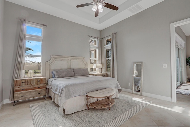 tiled bedroom with ceiling fan and a tray ceiling