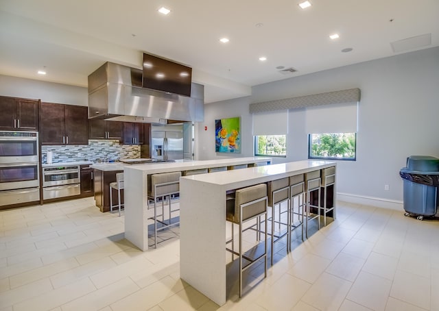 kitchen with tasteful backsplash, a breakfast bar, stainless steel appliances, wall chimney range hood, and a kitchen island