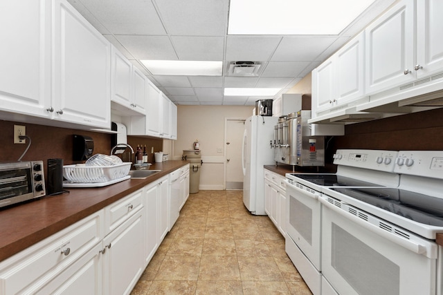 kitchen with white appliances, a paneled ceiling, butcher block countertops, white cabinets, and sink