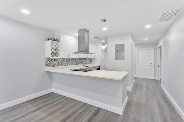 kitchen featuring kitchen peninsula, pendant lighting, electric panel, wall chimney range hood, and white cabinets