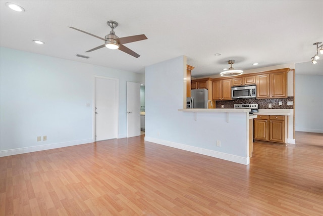 kitchen with stainless steel appliances, tasteful backsplash, kitchen peninsula, a kitchen bar, and light wood-type flooring