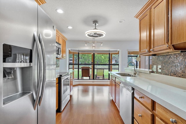 kitchen featuring sink, light wood-type flooring, a textured ceiling, tasteful backsplash, and stainless steel appliances