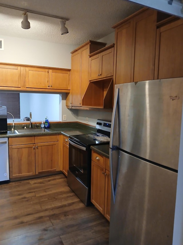 kitchen with a textured ceiling, appliances with stainless steel finishes, track lighting, dark wood-type flooring, and sink