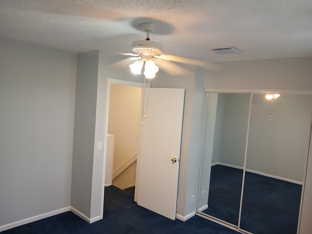 unfurnished bedroom with ceiling fan, dark carpet, a closet, and a textured ceiling