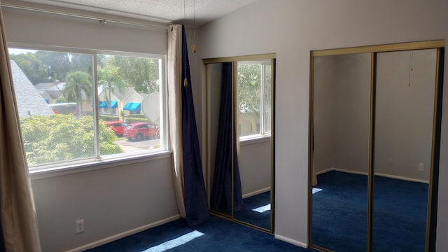 unfurnished bedroom featuring multiple closets, dark carpet, a textured ceiling, and lofted ceiling