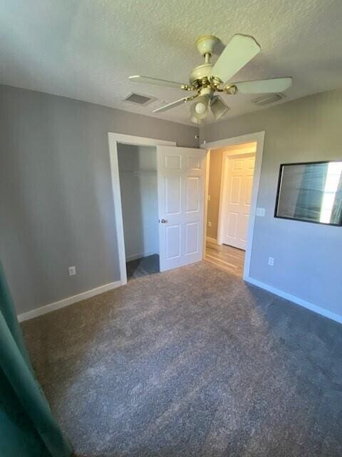 unfurnished bedroom with ceiling fan, a closet, a textured ceiling, and dark colored carpet