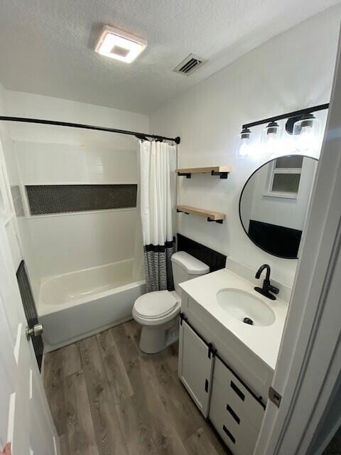 full bathroom featuring vanity, hardwood / wood-style flooring, toilet, a textured ceiling, and shower / tub combo with curtain