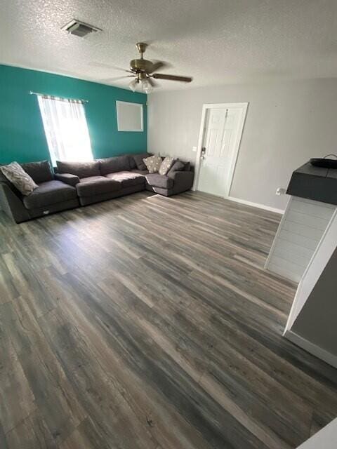 living room featuring a textured ceiling, ceiling fan, and dark wood-type flooring