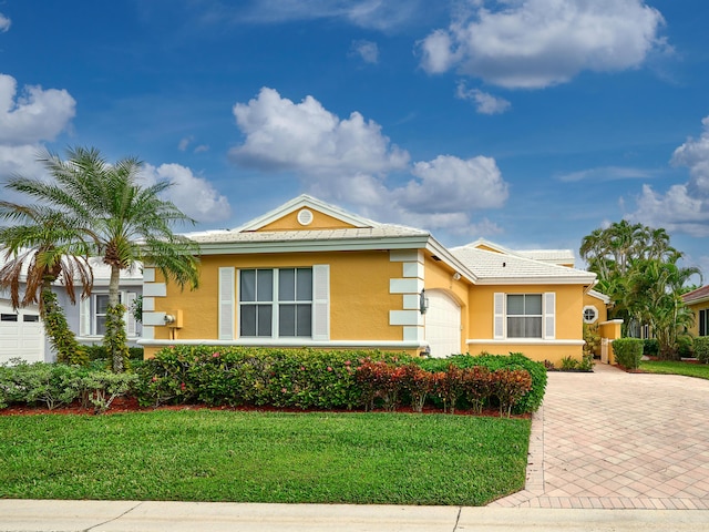 view of front of house featuring decorative driveway, a front lawn, an attached garage, and stucco siding