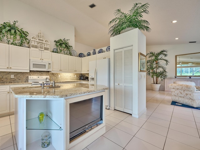 kitchen with decorative backsplash, white appliances, an island with sink, and vaulted ceiling