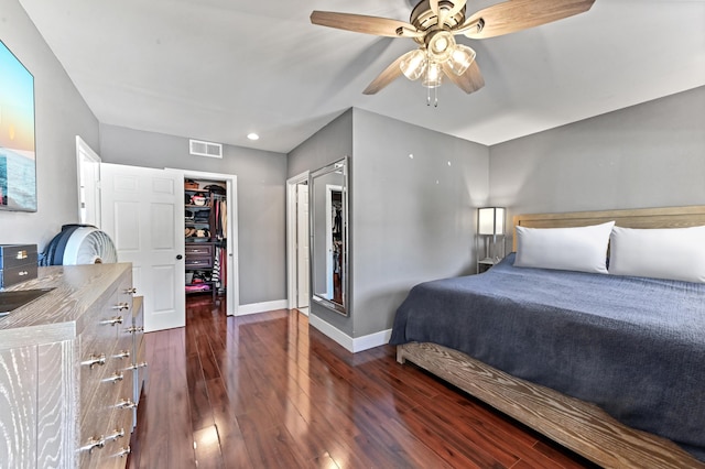 bedroom featuring a walk in closet, dark hardwood / wood-style floors, and ceiling fan