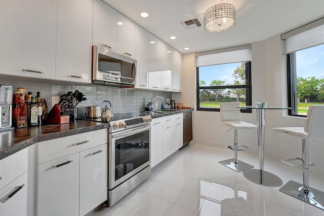 kitchen with sink, appliances with stainless steel finishes, tasteful backsplash, light tile patterned flooring, and white cabinetry