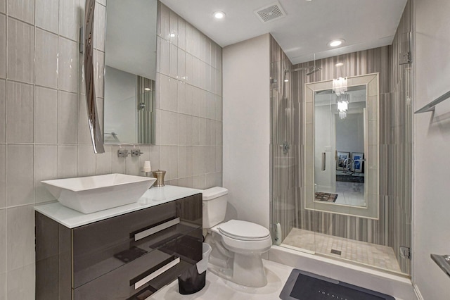 bathroom featuring vanity, toilet, a shower with door, and tile walls