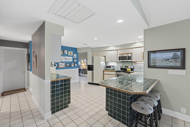 kitchen featuring kitchen peninsula, a kitchen bar, stainless steel appliances, light tile patterned floors, and tile countertops