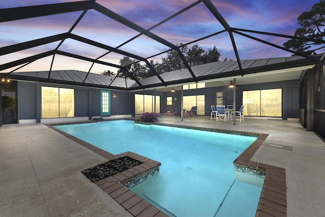 pool at dusk with glass enclosure, ceiling fan, and a patio