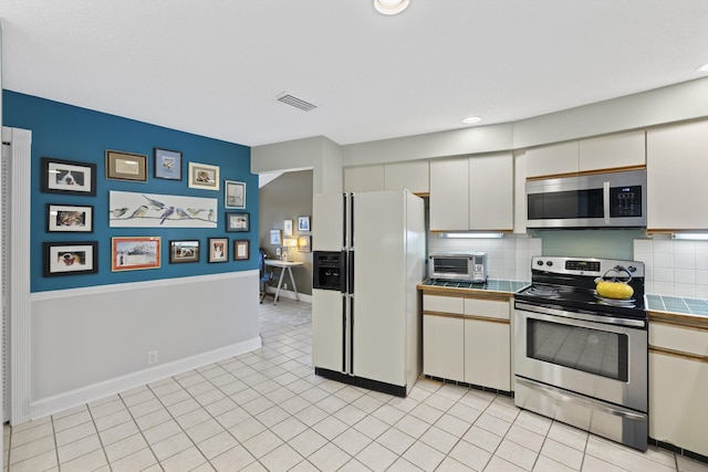 kitchen with white cabinetry, stainless steel appliances, backsplash, tile countertops, and light tile patterned floors