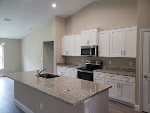 kitchen featuring white cabinets, appliances with stainless steel finishes, a center island with sink, and light stone countertops