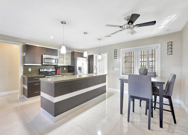 kitchen featuring backsplash, dark stone counters, hanging light fixtures, dark brown cabinets, and stainless steel appliances