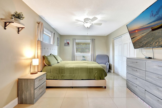 bedroom with ceiling fan, a closet, light tile patterned floors, and a textured ceiling