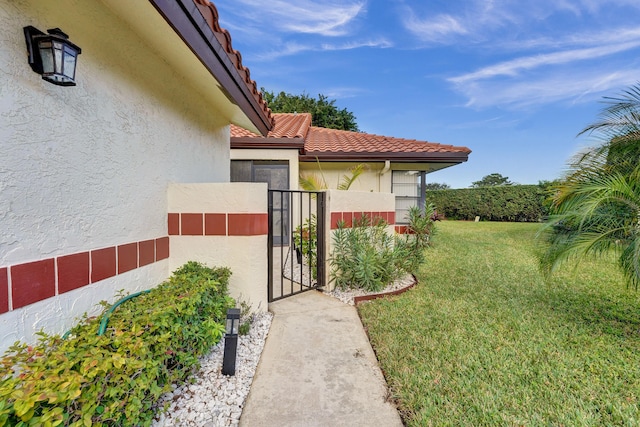 view of home's exterior featuring a tiled roof, a gate, a lawn, and stucco siding