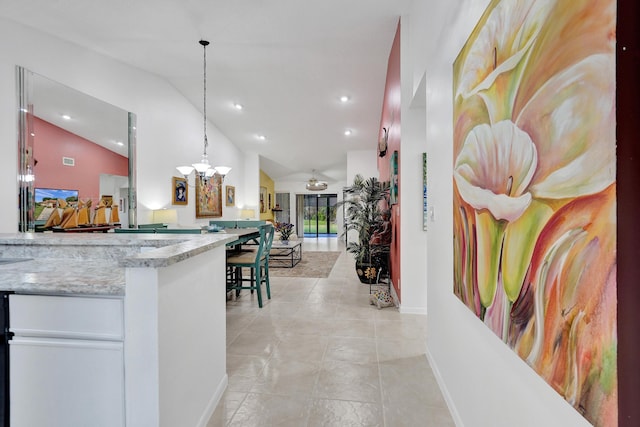 kitchen featuring lofted ceiling, an inviting chandelier, light stone counters, white cabinets, and decorative light fixtures