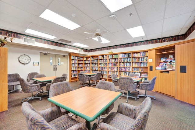 carpeted office space with a drop ceiling, wooden walls, built in features, and ceiling fan