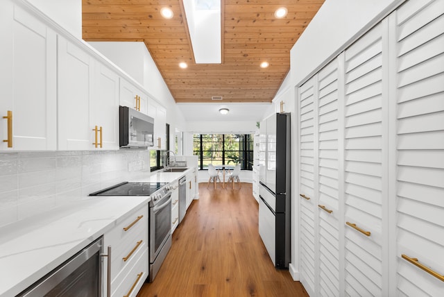 kitchen with wood ceiling, appliances with stainless steel finishes, white cabinetry, vaulted ceiling with skylight, and wine cooler