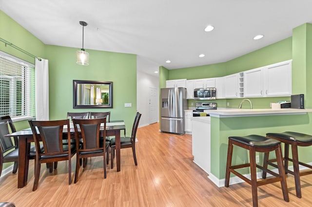 kitchen with light hardwood / wood-style floors, kitchen peninsula, white cabinetry, hanging light fixtures, and stainless steel appliances