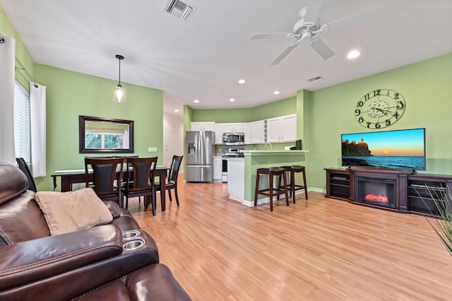 living room featuring ceiling fan, sink, and light hardwood / wood-style flooring