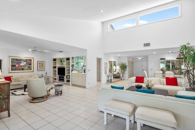 living room with a textured ceiling, a towering ceiling, ceiling fan, and light tile patterned flooring