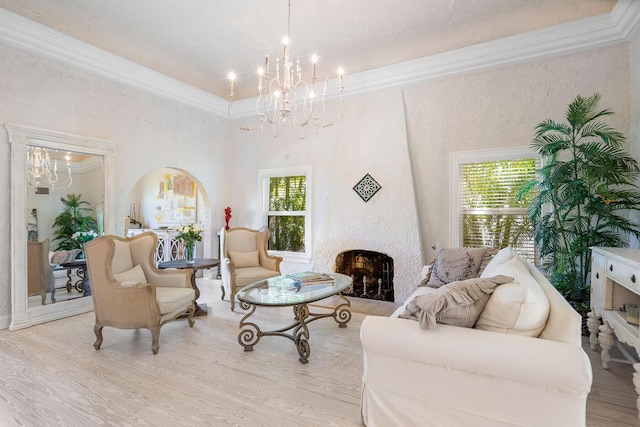 living area featuring light wood finished floors, a fireplace, arched walkways, and crown molding